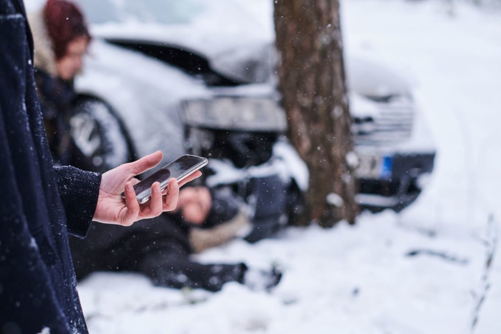 Man is holding mobile phone to call ambulance while woman is checking injured male after a car accident.